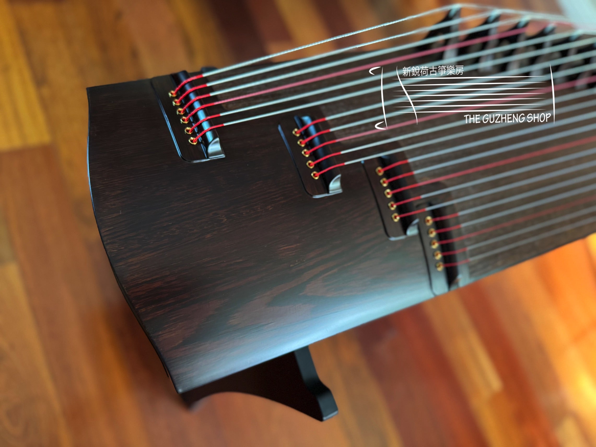 Close-up of a Guzheng on a wooden surface with 'The Guzheng Shop' branding.